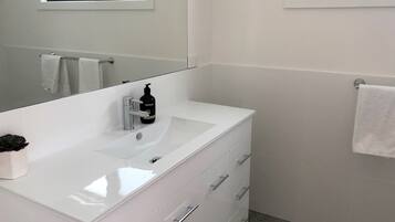 A modern bathroom with a white vanity, a large mirror, and a small plant on the counter.