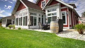 A two-story house with a red and white exterior, large windows, and a patio area with a table and chairs. - Peaceful, Modern Lake Cottage/A Sunny Retreat @ The Cottages on Osoyoos Lake 🌅 (Oliver)