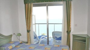 Ein Zimmer mit einem Bett, einem Schreibtisch und einem Stuhl. Durch eine Schiebetür hat man Blick aufs Meer.