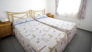 Ein Zimmer mit zwei Einzelbetten, einem Holzkopfstück, einem Nachttisch mit Lampe und einem Fenster mit Vorhängen.