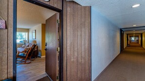 Un couloir d’hôtel avec des lambris en bois, un sol recouvert de moquette et un espace détente avec des chaises et une table.