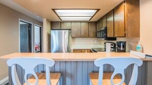 Une cuisine dotée de meubles en bois, d’un réfrigérateur en acier inoxydable, d’un four à micro-ondes et d’un coin bar avec deux chaises blanches.
