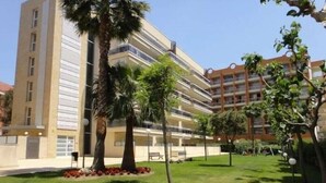 Un immeuble résidentiel à plusieurs étages, doté de balcons, entouré d’une pelouse bien entretenue et de palmiers.