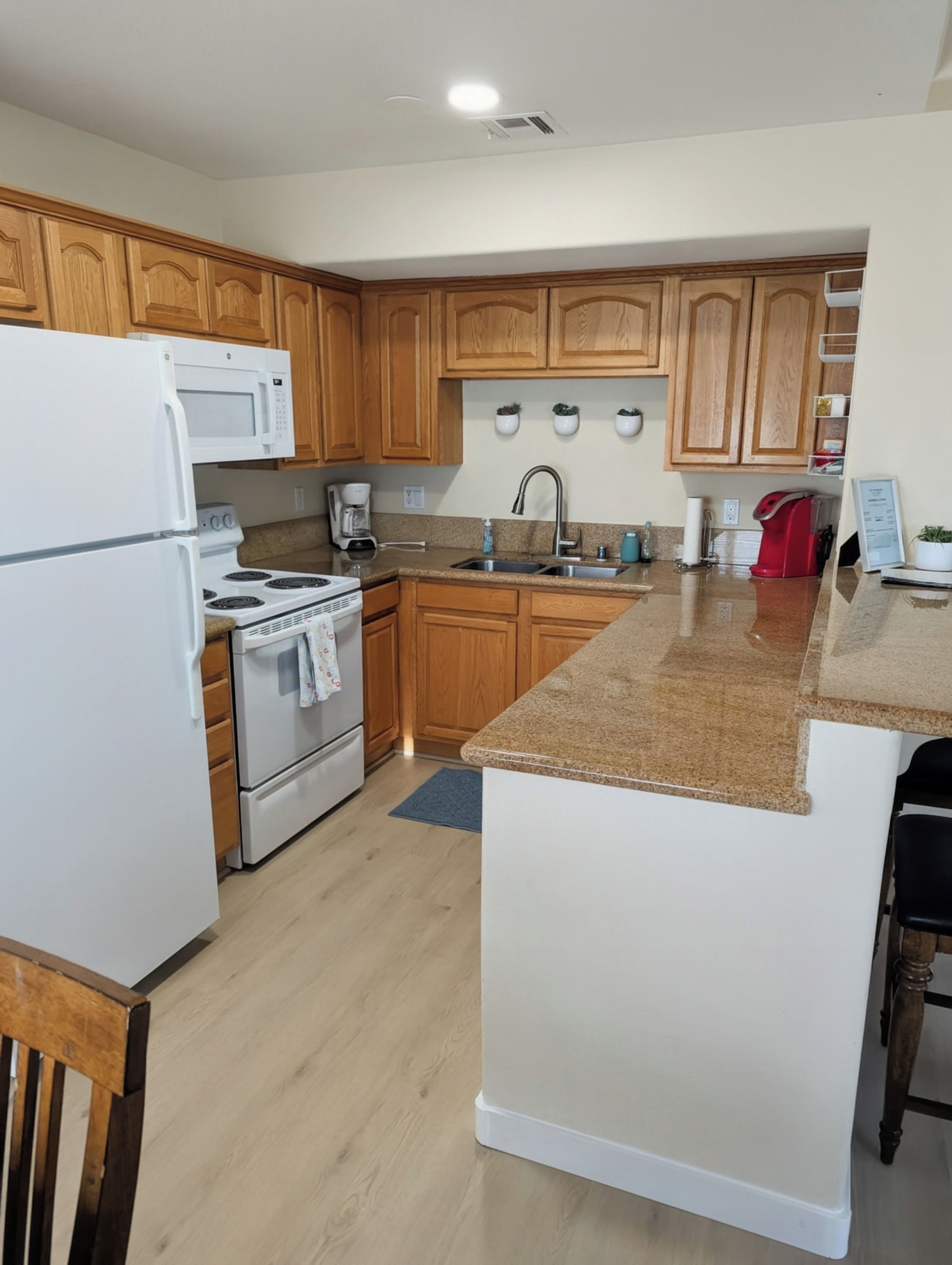 A kitchen with wooden cabinets, a white refrigerator, a stove, a sink, and a granite countertop.