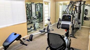 Ein Fitnessstudio mit Trainingsgeräten, einer Spiegelwand und einem Fenster mit Jalousien.