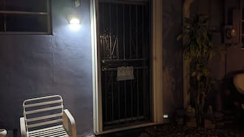 A house exterior at night with a metal gate, a bench, and a potted plant.