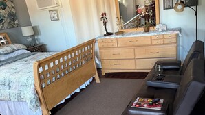 Une chambre à coucher comprenant un lit, une commode en bois, une coiffeuse avec un miroir, un canapé et un ventilateur de plafond.