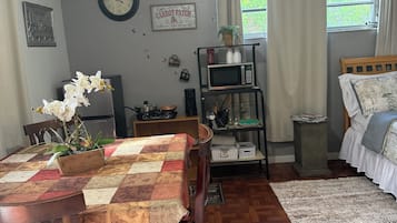 Una habitación acogedora con una mesa de madera, una cama con colcha estampada, un reloj en la pared y una ventana con cortinas.