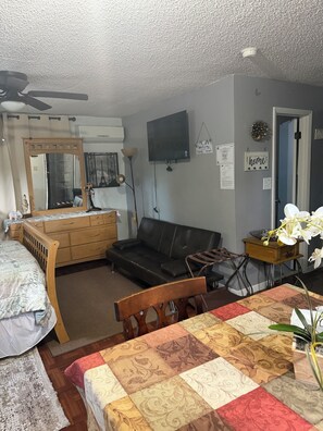 A room with a bed, a dresser, a sofa, a television, and a table with a patterned tablecloth.