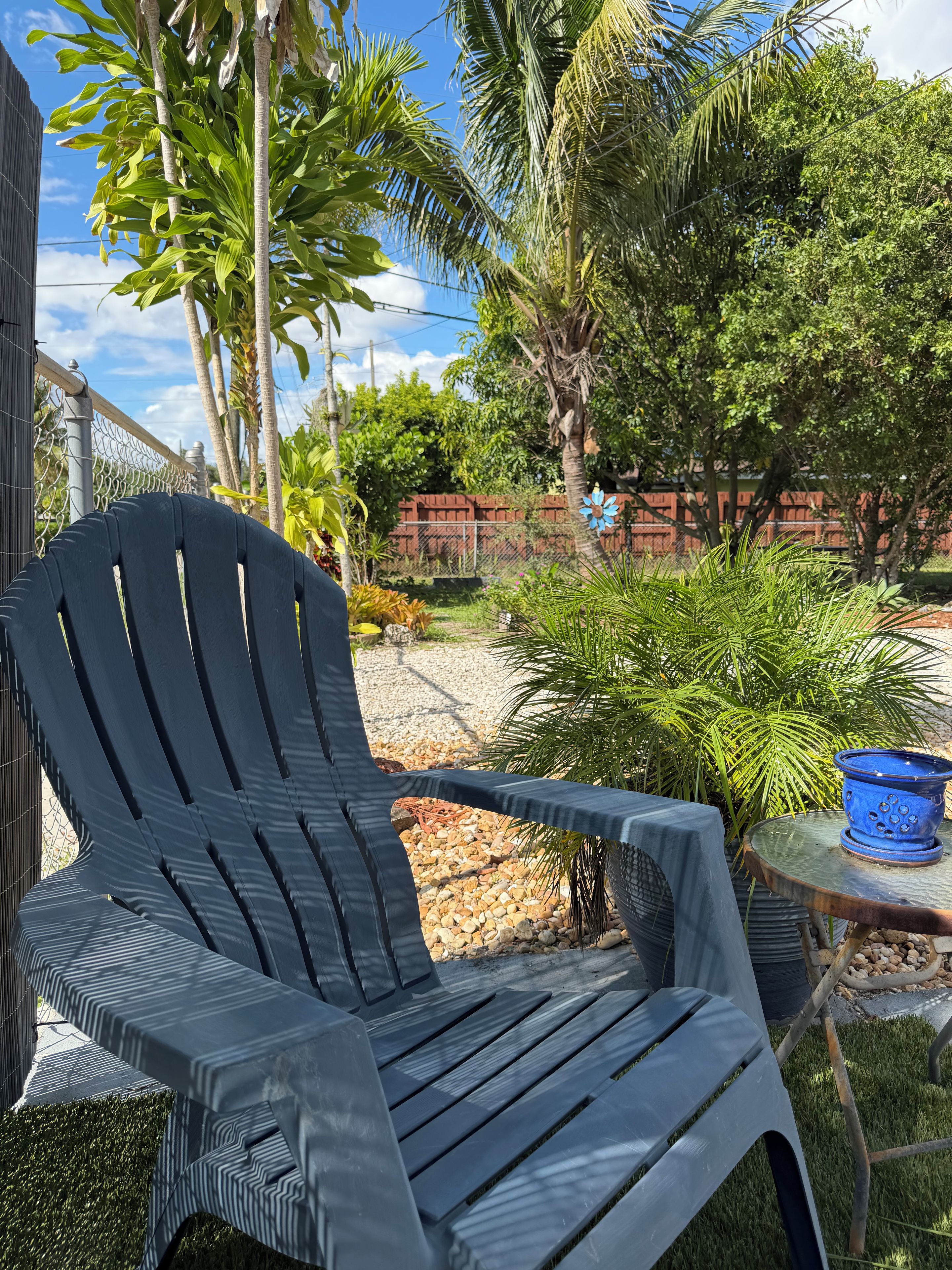 A black plastic chair and a small table with a blue pot in a garden setting.