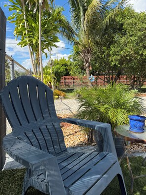 A black plastic chair and a small table with a blue pot in a garden setting.