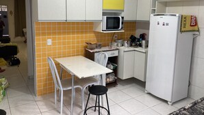 Eine kleine Küche mit einem weißen Kühlschrank, einer Mikrowelle und einem Essplatz mit zwei Stühlen.