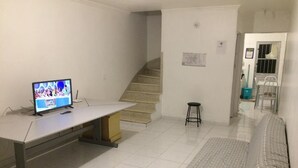 Ein Zimmer mit einem Bett, einem Schreibtisch mit Computer, einem Stuhl, einem kleinen Hocker und einer Treppe.