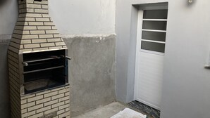 Ein gemauerter Außenofen neben einer weißen Tür mit Fenster, und einer wandmontierten Leuchte.