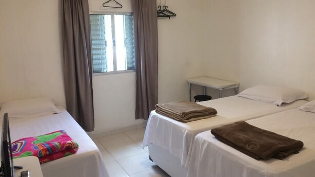 Ein Hotelzimmer mit zwei Betten, einem kleinen Tisch, einem Stuhl und einem Fenster mit Vorhängen.