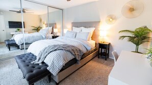 Un dormitorio moderno con una cama grande, un ventilador de techo, un espejo y un escritorio pequeño con una silla.