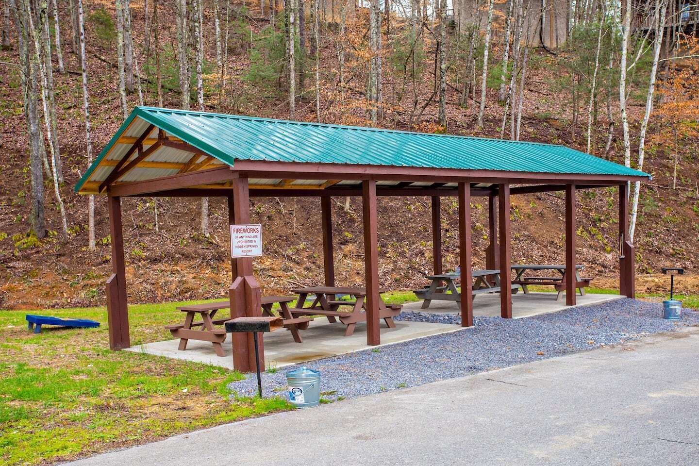 A covered picnic area with benches and picnic tables, surrounded by a forest.