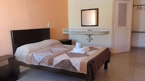 A neatly made bed with a patterned bedspread, a bedside table, a wall-mounted mirror, and a small sink with a towel. - Hotel Jireh (Bacalar)