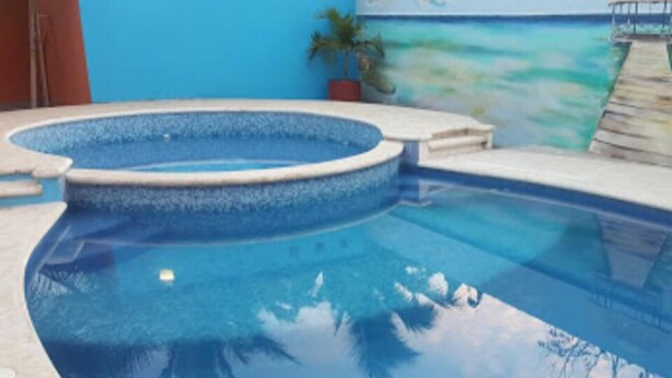 A swimming pool with a curved edge, a small deck area, and a view of the ocean in the background. - Hotel Jireh (Bacalar)