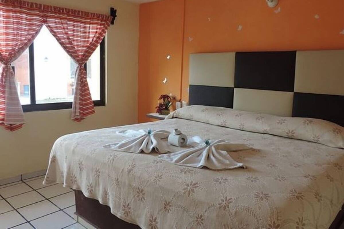 A hotel room with a bed, a nightstand, and a window with curtains.