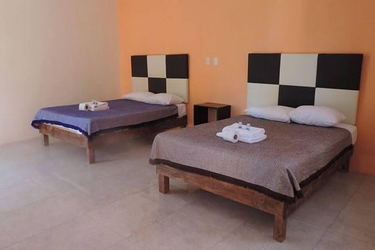 Two single beds with wooden frames and headboards, a small bedside table, and a plain orange wall.