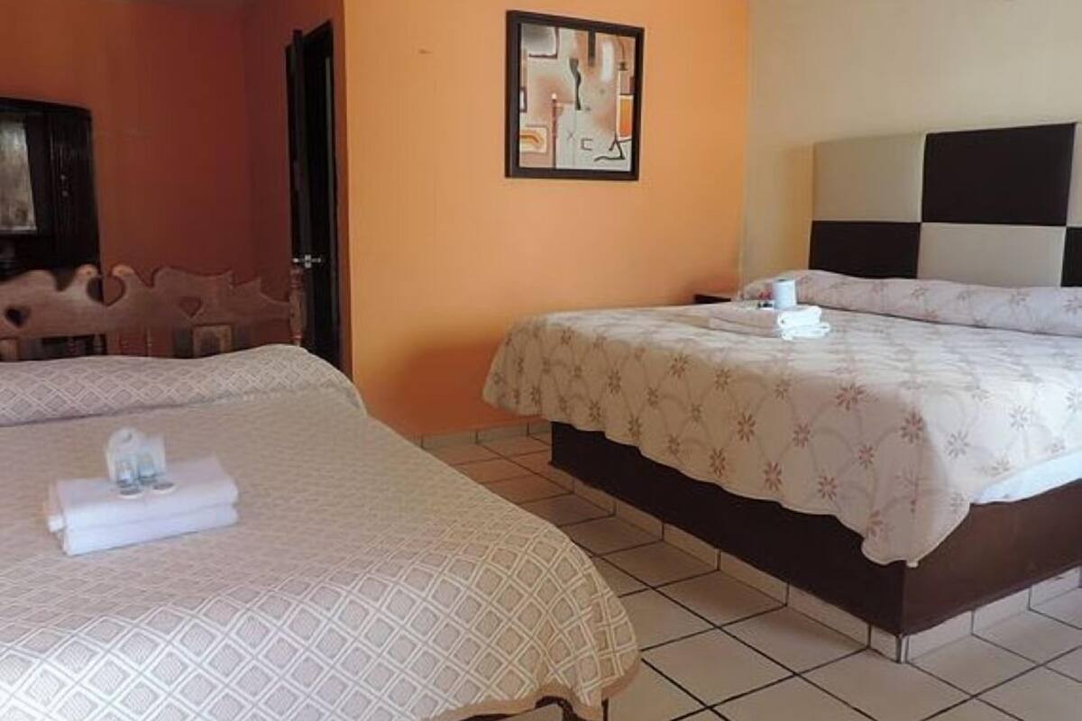 A hotel room with two beds, a painting on the wall, and a door.