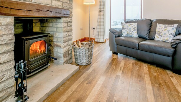 A cozy living room with a stone fireplace, a leather sofa, and a large window. - Woodland's Clough - UK32387 (Don View, near Dunford Bridge)