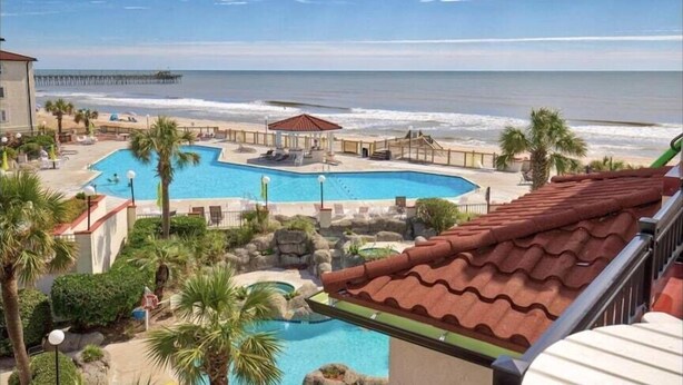 Un resort con una amplia piscina, vista a la playa y un muelle al fondo.