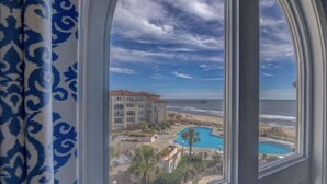Vista desde una ventana hacia una playa, una piscina y un edificio de varios pisos.