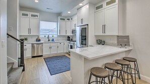 A modern kitchen with white cabinetry, stainless steel appliances, a marble island, and bar stools.
