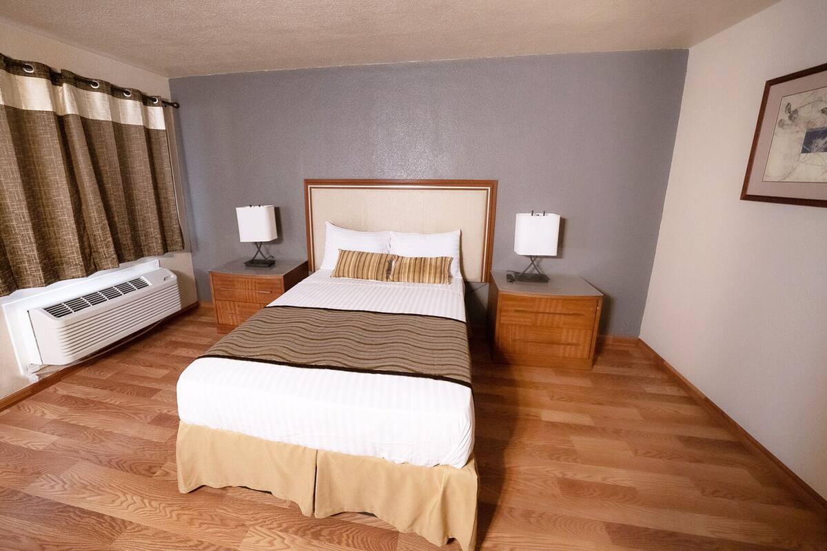 A hotel room with a bed, two bedside tables with lamps, a heater, and a framed picture on the wall.