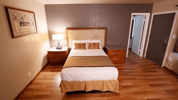 Une chambre d’hôtel avec un lit, des tables de chevet, une lampe et un tableau encadré au mur.