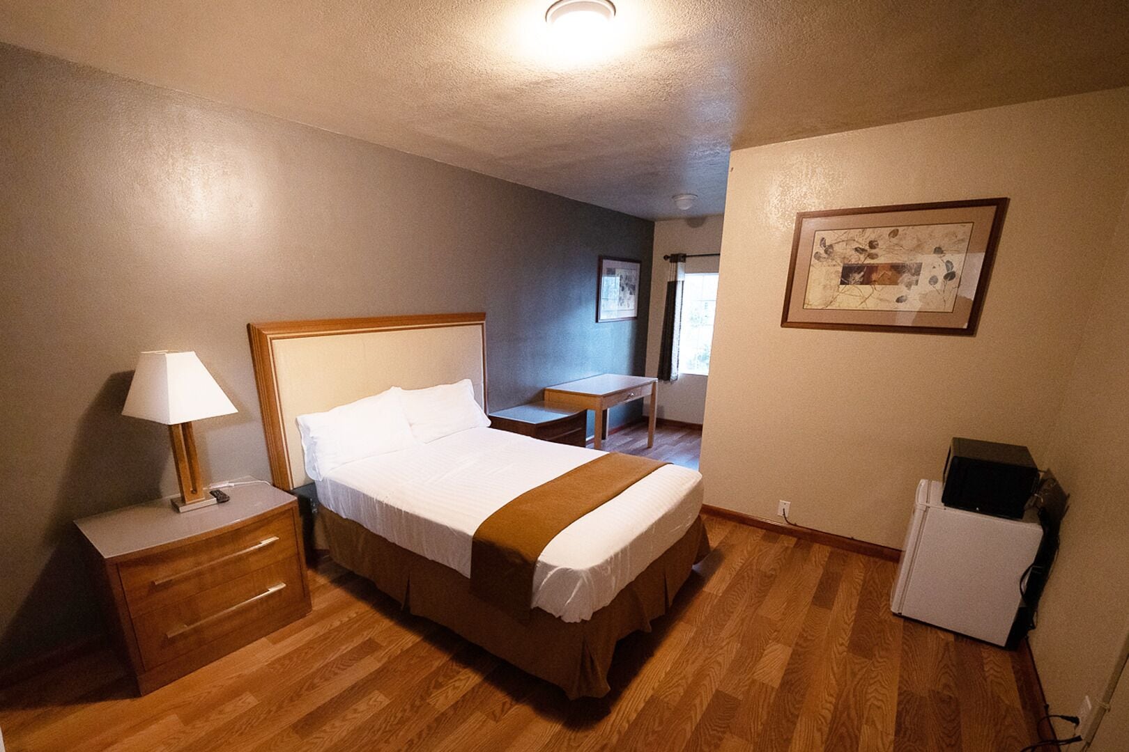 A hotel room with a bed, bedside table, lamp, and a small desk.