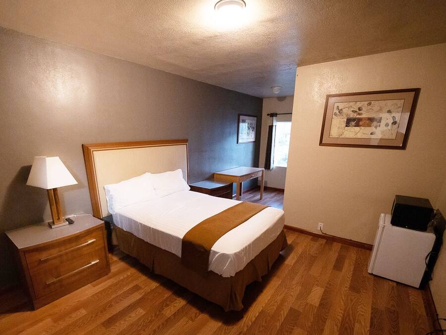 A hotel room with a bed, bedside table, lamp, and a small desk.