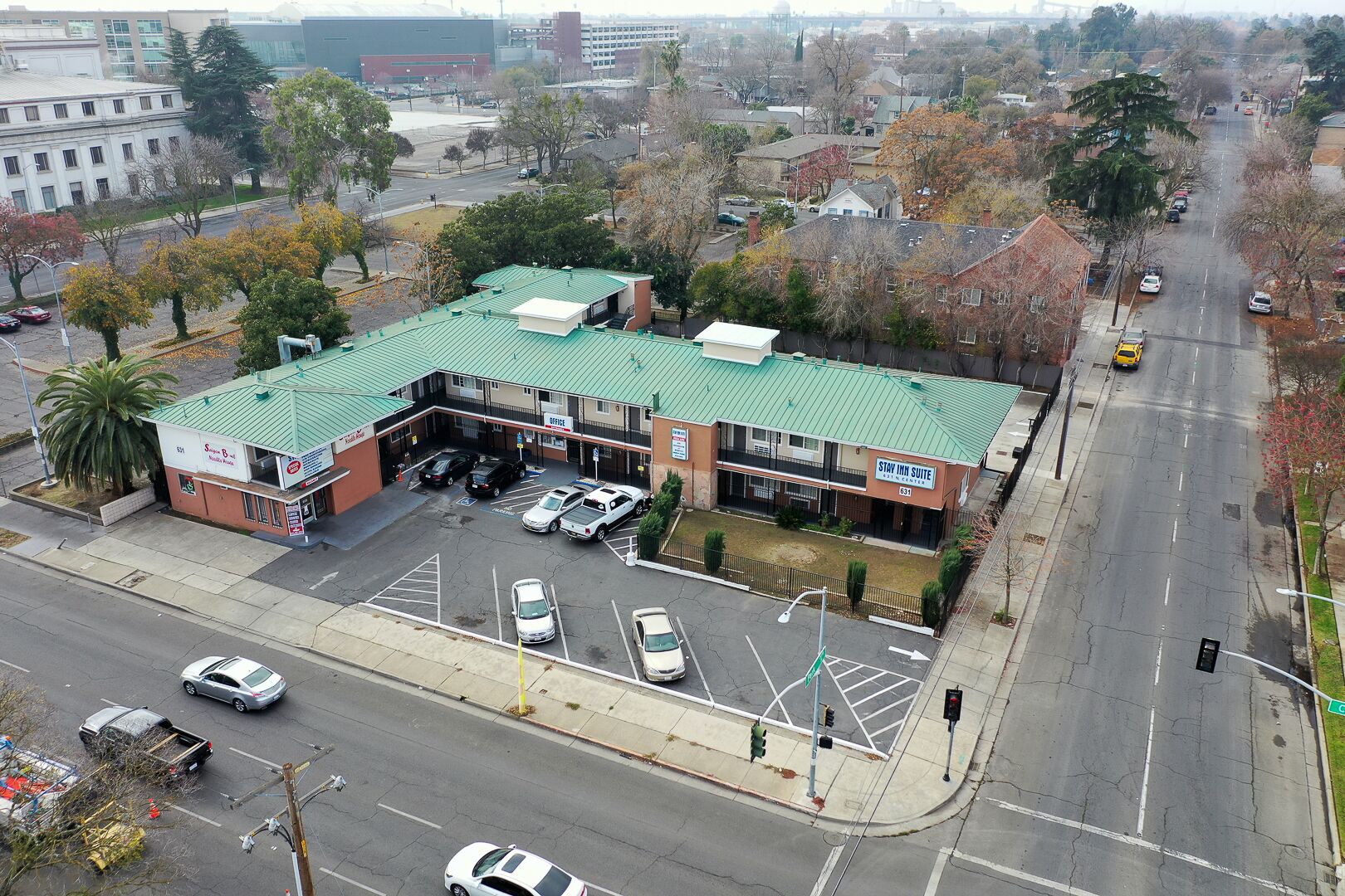 A Stay Inn Suite building with a green roof, parking lot, and a street view.