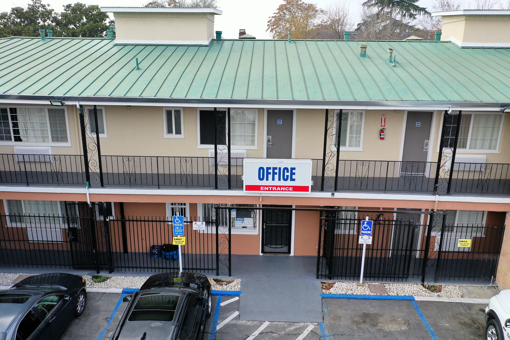 A multi-story building with an 'OFFICE' sign at the entrance, parking spaces, and a gated entrance.