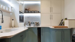 A modern kitchen with white cabinets, a stainless steel sink, and a built-in dishwasher. - Mac Shack Cottage - UK32376 (Ashen, near Clare)