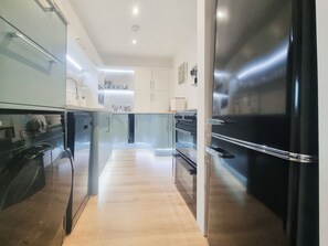 A modern kitchen with stainless steel appliances, wooden flooring, and white cabinetry. - Mac Shack Cottage - UK32376 (Ashen, near Clare)