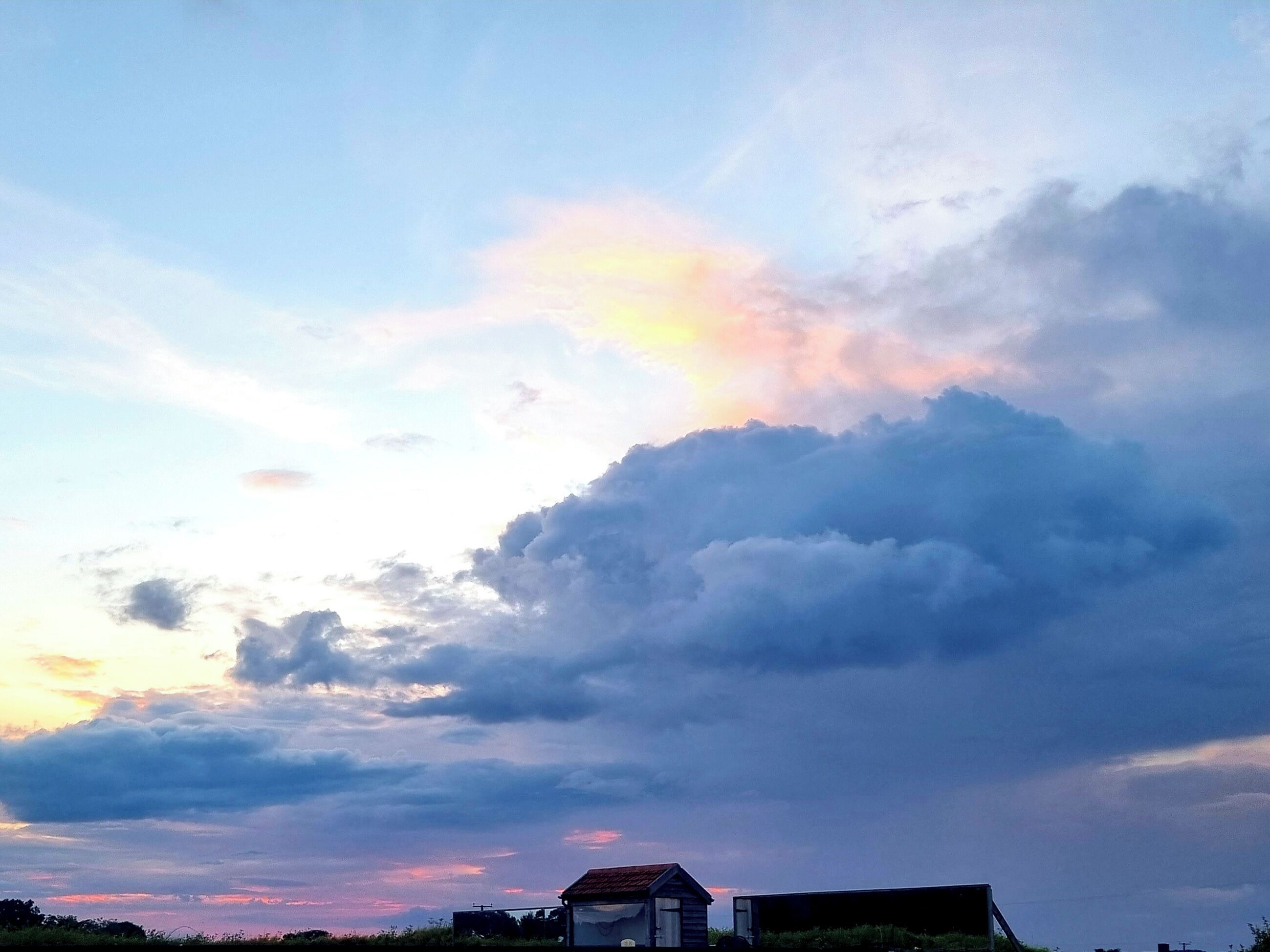 A rural landscape with a large cloud formation and a small building with a red roof.