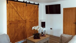 A living room with a wooden sliding door, a fireplace, a television mounted on the wall, and a sofa. - Mac Shack Cottage - UK32376 (Ashen, near Clare)
