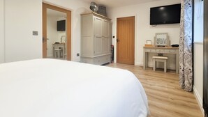 A bedroom with a large bed, a wardrobe, a desk, and a TV mounted on the wall. - Mac Shack Cottage - UK32376 (Ashen, near Clare)