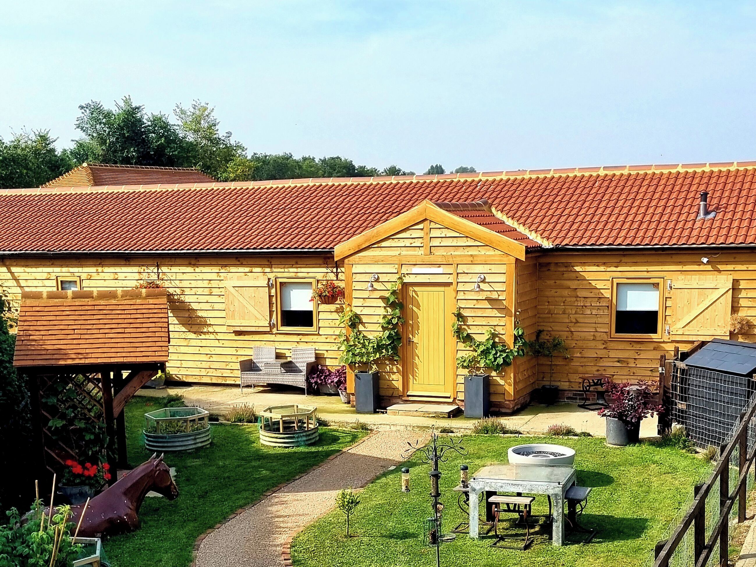 Ein Holzhaus mit rotem Ziegeldach, einer Haustür und einer kleinen Veranda mit Korbmöbeln.