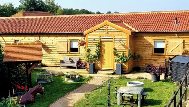 A wooden house with a red-tiled roof, a front door, and a small porch with wicker furniture. - Mac Shack Cottage - UK32376 (Ashen, near Clare)