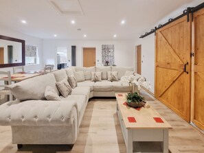 A modern living room with a sectional sofa, a wooden coffee table, and a large sliding barn door. - Mac Shack Cottage - UK32376 (Ashen, near Clare)