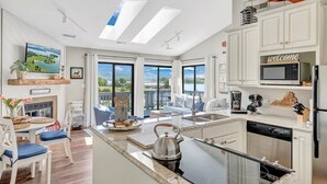A modern kitchen with a central island, a dining area with a view, and a living space with a sofa and a TV. - Moondance at BERNARD’S LANDING (moneta)