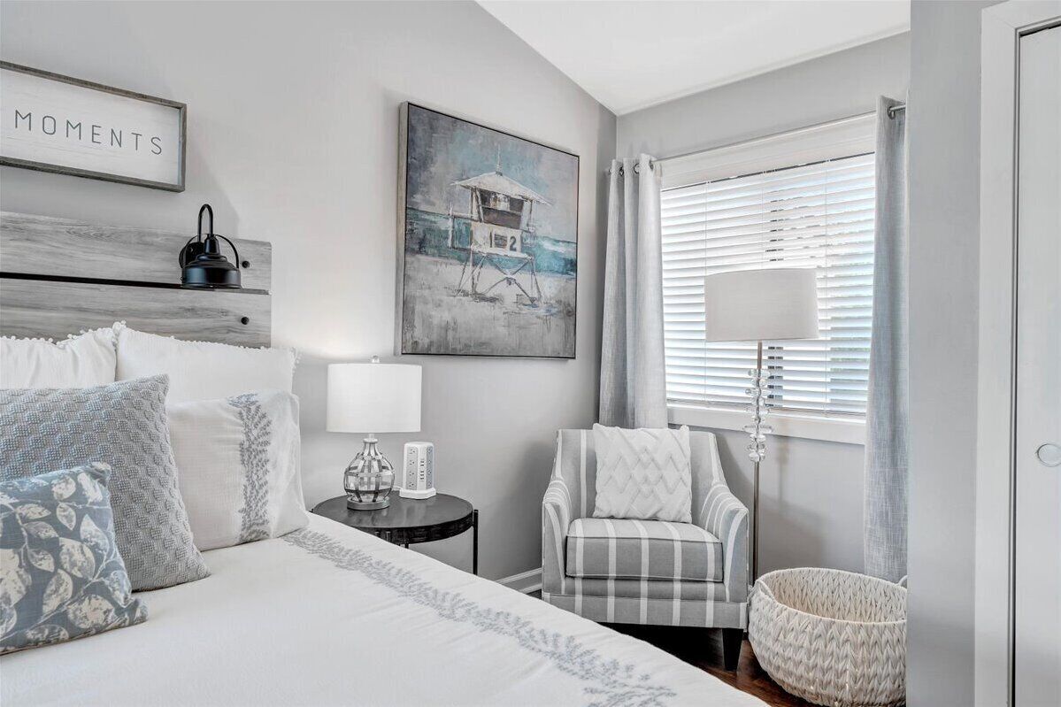 A bedroom with a bed, bedside table, lamp, chair, and artwork.