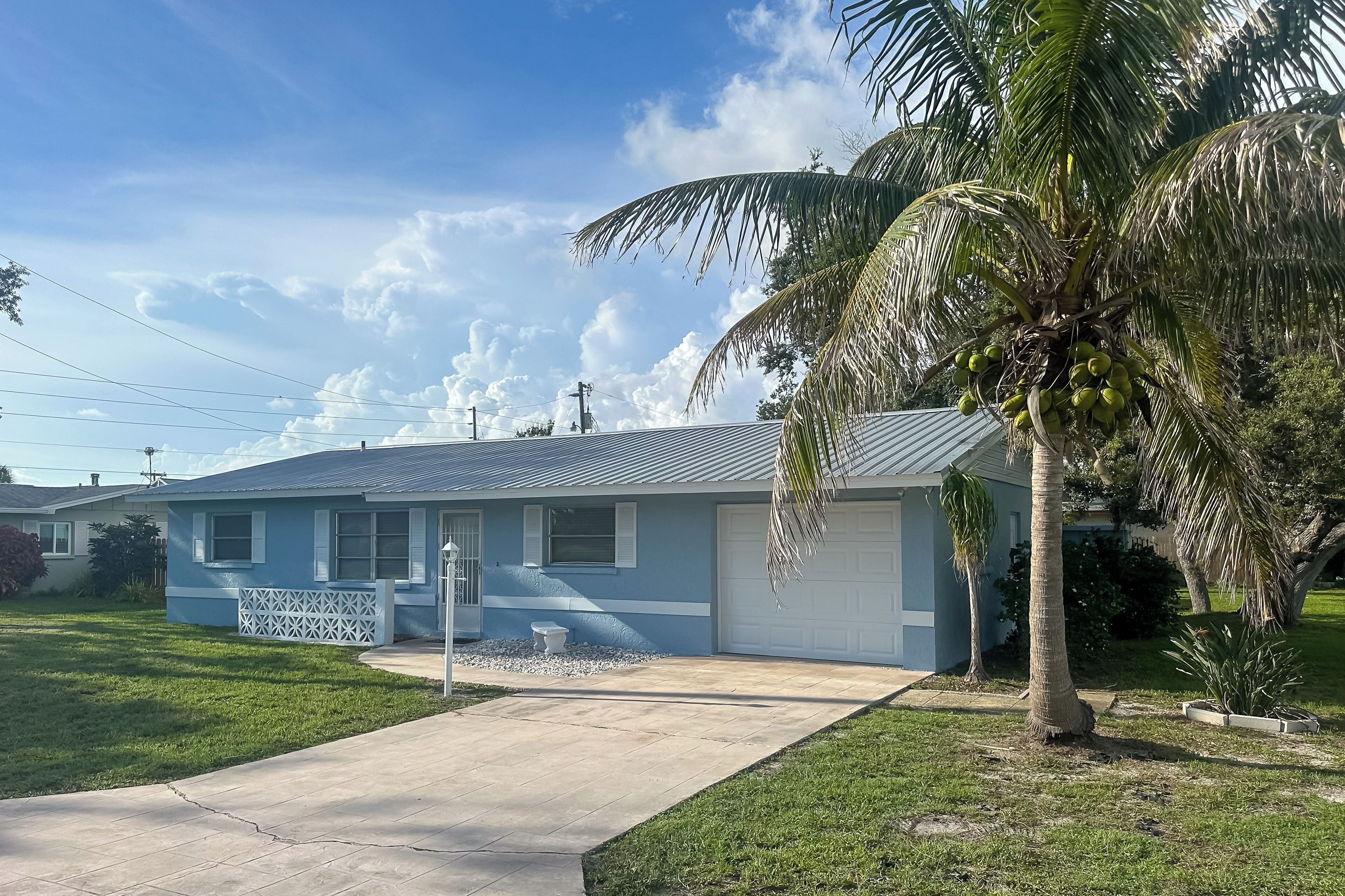 A single-story house with a garage, a lawn, and a palm tree.