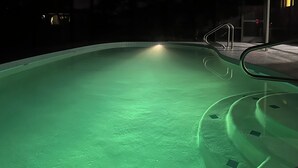 Una piscina con un ligero tono verdoso, una escalera de metal y una puerta al fondo.