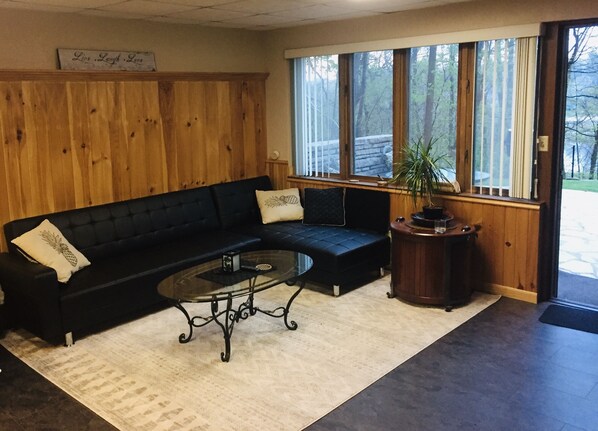 A black sectional sofa with two decorative pillows, a glass coffee table, and a wooden side table with a potted plant.