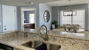 A kitchen with granite countertops, a stainless steel sink, and a dining area with a chandelier.